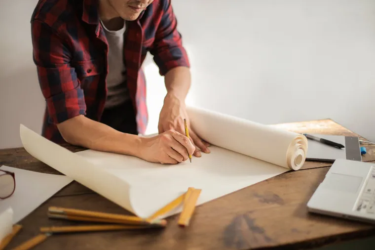 Male architect drafting blueprints on a large paper roll